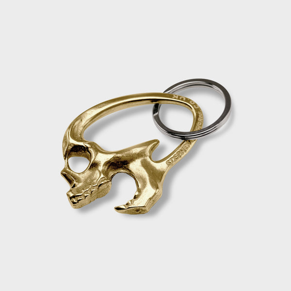 A side view of a polished brass skull bottle opener. It has its mouth open.