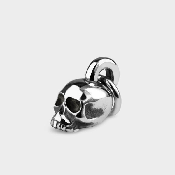 A side view of a silver skull and crossbone charm.