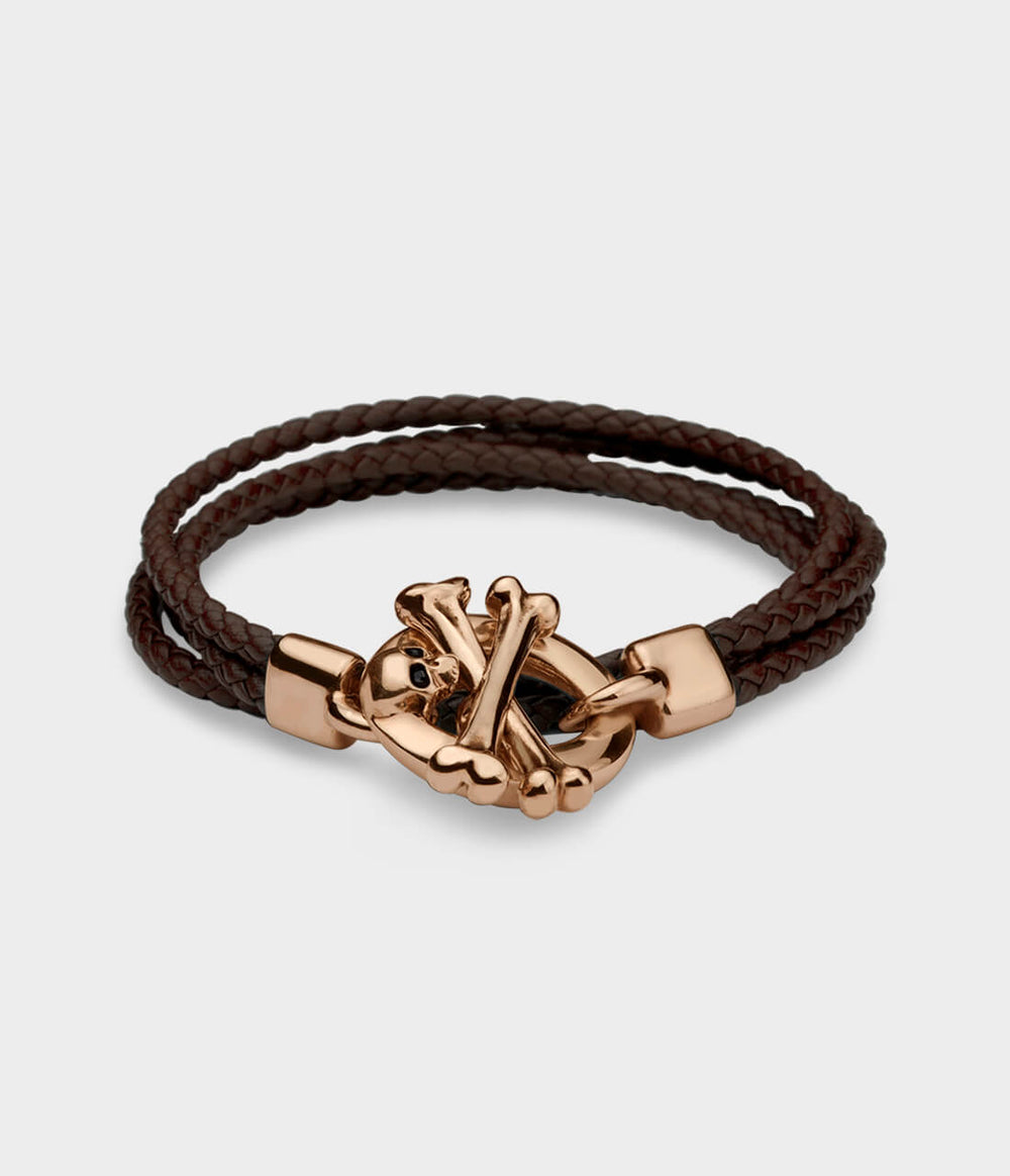 A brown leather double strand  bracelet with a detailed rose gold skull and crossbone T bar catch with blue sapphire eyes